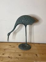 Side view of the green heron garden ornament showing detailed feather and scale patterns and thin legs attached to a round base.