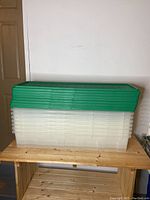 Side and front views of stacked translucent clear plastic storage totes with green lids stacked separately on top.