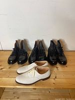 Four pairs of men's shoes on wooden surface: three black leather police boots and one pair of white suede dress shoes, all size 10.5.