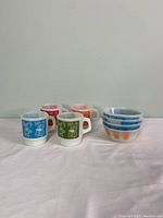Photo showing 4 colorful milk glass mugs and 4 matching milk glass bowls with cooking themed prints.