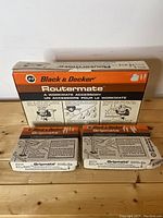 Photo showing boxed Black & Decker Routermate and two boxes of Gripmate accessories on a wooden surface