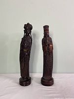 Pair of dark brown Asian-style figurine statues, male and female, standing side by side on round bases, 16 inches tall.