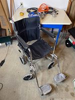 Front view of manual wheelchair showing black seat and armrests, footrests and wheels.