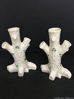 Front view of two Belleek porcelain vases with tree stump shape and shamrock decoration against black background.