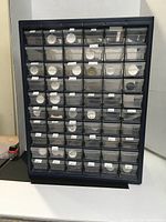 Front view of blue cabinet with 56 transparent small drawers labeled and containing small items including seed beads.