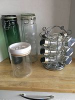 Set of three glass canisters with lids and a rotating spice rack with spice jars arranged on a countertop.