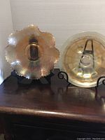 Two carnival glass bowls placed on display stands, showing iridescent gold and pink colors and scalloped edges.