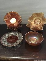 Stack of carnival glass pieces showing ruffled edges and iridescent amber coloring with floral embossing. Clear souvenir dish bottom-left with 'Toronto Exhibition 1927' in center.