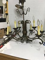 Metal chandelier with 8 candle-style lights and crystal decorations, on white background showing some wear and missing crystals present.