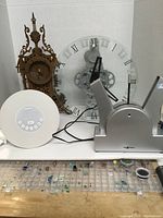 Four clocks on a shelf: wooden carved clock, clear gear clock, white digital clock, silver Nexxtech message clock.