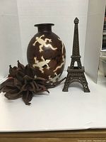 Image showing large Peruvian jug decorated with cream-colored lizard designs and metal Eiffel Tower tea light holder side by side on a white surface.