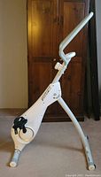 Side view of the white Fitnation vertical cycle trainer showing its upright design, pedals, and handlebar.