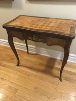 Front view of folded card table showing inlaid wood parquetry top and ornate carved legs with gilded accents.