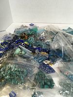 Photo showing large assortment of blue beads of different shapes and sizes inside small resealable clear plastic bags scattered together on a white surface.