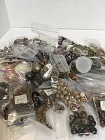 Photo showing a large quantity of various brown beads in sealed plastic bags, assorted by size and type, suitable for crafting or jewelry making.