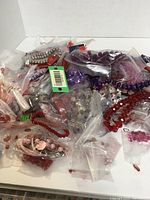 Photo of the large assortment of red and purple beads sorted loosely and in plastic zip bags, showing the variety, colors, and bead types for crafts.