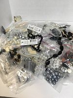 Photo showing multiple plastic bags filled with assorted black, white, silver, and translucent beads in various shapes and sizes.
