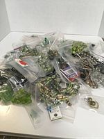 Top view of large assortment of green and metallic beads in mostly plastic bags spread on white surface