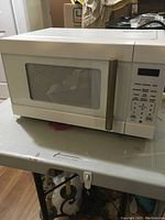 White microwave oven with a dark glass door and gold vertical handle, digital control panel with display and keypad on the right side.