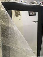 Close up image of the top left corner of the mirror showing dark brown wood frame with minor scratches and bubble wrap partially covering it.