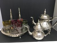 Photo of a Moroccan tea set including a silver teapot, silver kettle with lid, six colored glasses in decorative silver holders, and a round silver tray.