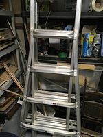 Photo of the silver aluminum multi-level ladder showing multiple rungs, hinges, and adjustable design in a workshop environment.