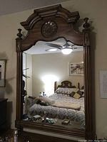 Full view of the large ornate pecan wood mirror hung on a bedroom wall, showing carved frame details and reflection of the room.