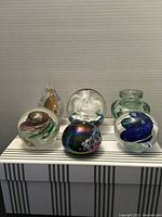 Front view of six glass paperweights with various internal designs and shapes.