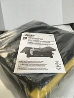 Photo showing the OEP tile saw wrapped in plastic packaging with the instruction manual on top.