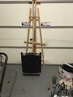 Photo showing tall wooden easel standing upright with portable black easel folded down in front of it.