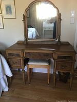 Front view of vintage wooden vanity with arched mirror and matching stool placed underneath.