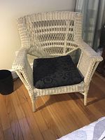 Cream-colored real wicker chair with woven design, shown with black cushion in place.