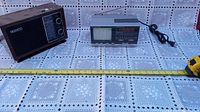 Sony portable radio and Emerson B/W TV radio placed on a patterned cloth with measuring tape for size reference