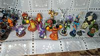 Front wide shot showing all 30 colorful Skylanders and related character figurines displayed on a fabric surface with a lace background.