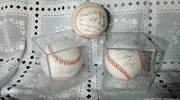 Three autographed baseballs, two in display cases, one without case, showing signatures from players including Dave Vera.