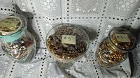Three jars wrapped in plastic, filled with assorted vintage costume jewelry displayed on crocheted lace tablecloth