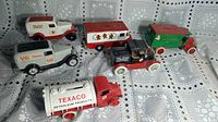 Six vintage style metal coin bank cars by ERTL with Coca Cola, Texaco and other branding, arranged on lace tablecloth.