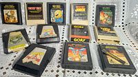 Overall view of 12 vintage Atari 2600 game cartridges arranged on lace cloth showing labels and wear.