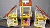 Full front view of the vintage original Barbie Dream House with two detachable side units and a tape measure showing the house height.