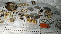 Wide view of all items on table showing belt buckles, lighters, cufflinks, money clips, and assorted jewelry.