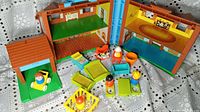 Full view of opened Fisher Price Play Family House with figures and furniture arranged inside and outside.