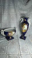 Photo showing both the cobalt blue Limoges urn and bowl with white handles and painted Victorian style scenes, set on white and gray lace patterned background.