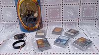 Overview of Magic The Gathering cards stacked and grouped, Lord of the Rings Gollum figure in packaging, dragon-themed wristwatch, and black bracelet displayed on lace tablecloth.