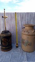 Vintage hand-painted milk jug lamp next to decorative floral milk jug container with measuring tape for scale