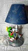 Side view of Marvin The Martian figurine on silver rocket base with blue lampshade featuring white line-art Looney Tunes characters