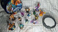 Wide view of 13 Skylanders character figures arranged by the Portal of Doom and carrying case on a white textured cloth