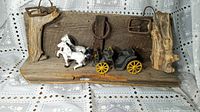 Wooden wall hanging with leather buckles and antique toy stagecoach drawn by two white horses in worn vintage condition.