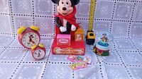 Photo showing all items together including two Mickey Mouse wind-up clocks, the Mickey magician figure on Magic Show stage, a Mickey Mouse snow globe, and a yellow tape measure for scale.