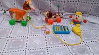 Photo showing the orange and white cow pull toy, Snoopy dog pull toy, toy calculator, and Humpty Dumpty figure all arranged on a white patterned cloth.