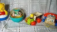 Photo showing four vintage Fisher-Price toys: yellow roly poly bear, Rollie Poly Time Ball, Jiffy dump truck, and pull-it telephone